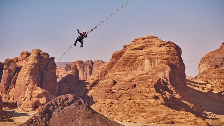 Adventurer soaring on the Giant Swing at AlUla's Adventure Hub, Saudi Arabia, flying through canyon terrain with breathtaking views, suspended 85 metres above the ground in a high-adrenaline 70-metre arc.