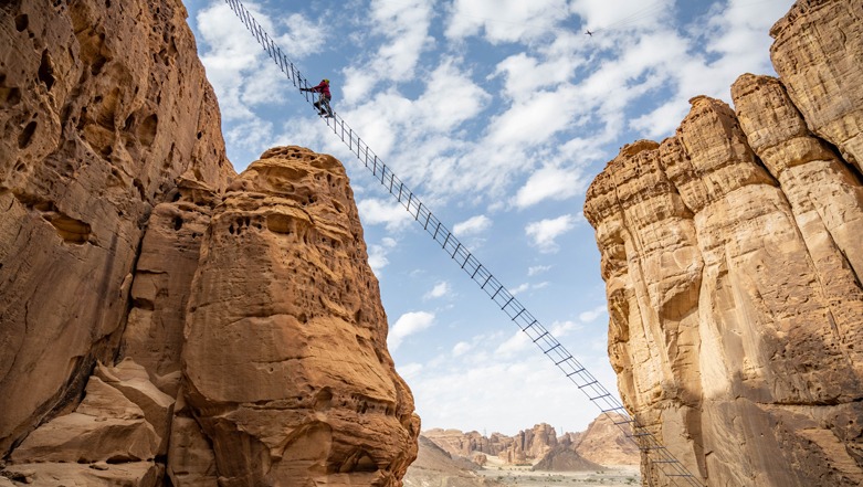 Adventure-seeker climbing the 45-metre AlUla Stairway ladder at Adventure Hub, Saudi Arabia, with epic mountain views, followed by a thrilling 150-metre zipline descent into the canyon.