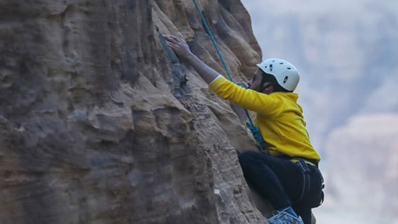 Person rock climbing in AlUla, Saudi Arabia, scaling cliffs and enjoying breathtaking desert views.