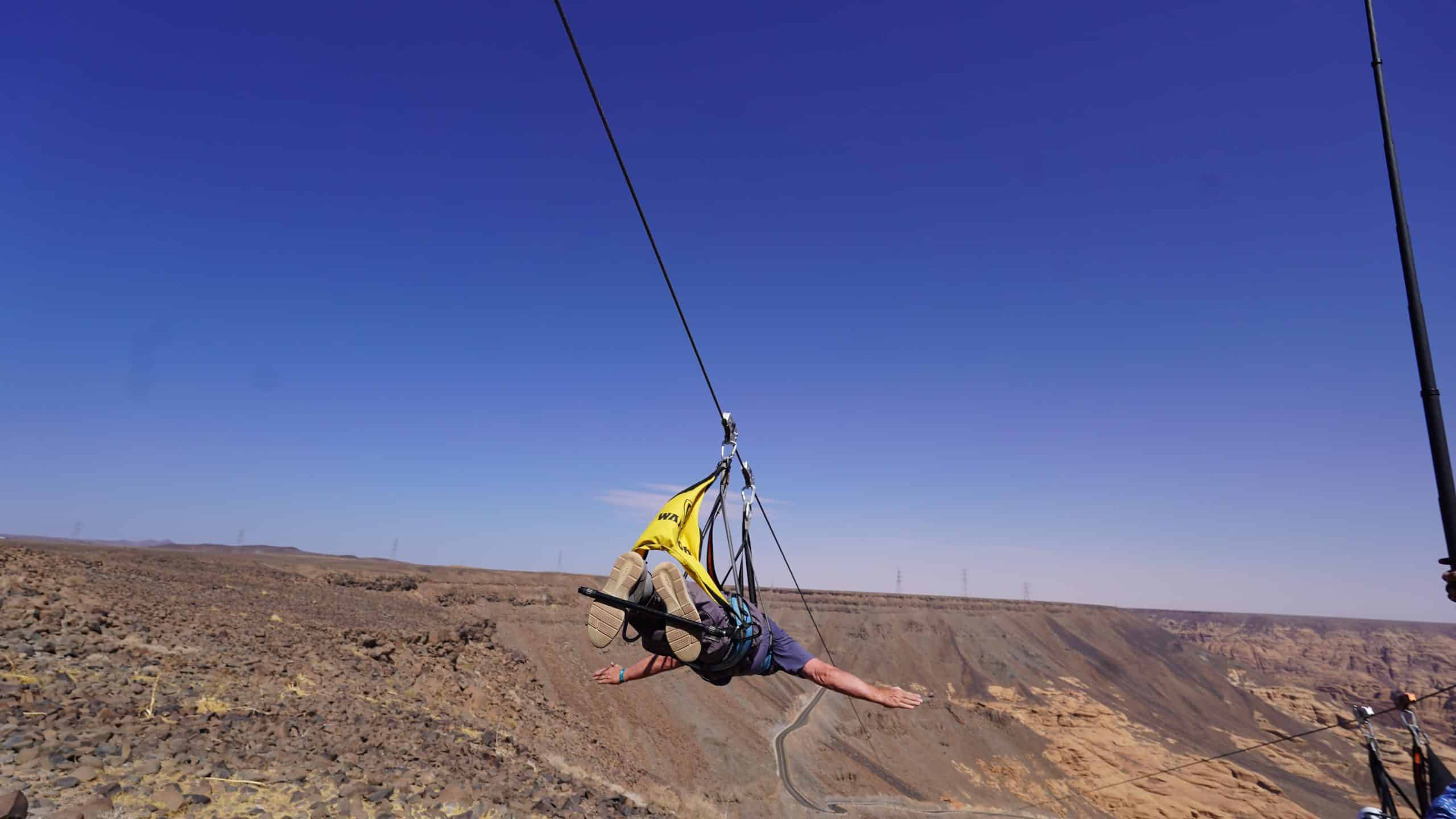 Participant gliding on a zipline over a scenic desert landscape, showcasing adventure and thrill in an outdoor setting